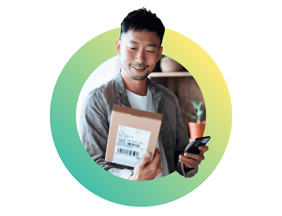 Smiling young asian man with smartphone receiving delivered packages from online purchases at home can't wait to unbox the purchases